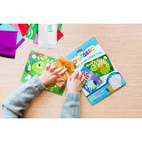 Child's hands applying gold foil to a green chameleon design from the Ooly Foil-Tastic art kit on a wooden table.