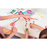 Two children crafting shrink art bracelets with colorful markers, pre-cut charms, string, and scissors on a white table.