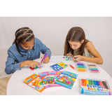 Two kids coloring Ooly Undercover Art Rainforest Fun pages with markers and brushes, surrounded by colorful sets.