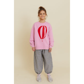Girl in pink organic cotton oversized sweatshirt with red hot air balloon print and checkered pants.