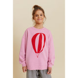 Smiling girl in an oversized pink organic cotton sweatshirt with a red hot air balloon print.