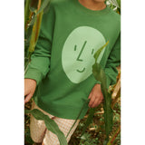 Kid's oversized green organic cotton sweatshirt with a light green potato face print, worn in a cornfield.