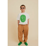 Boy wearing a beige organic cotton oversized t-shirt with a green potato face print, brown pants, and green shoes.