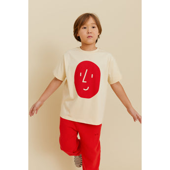 Boy wearing a light yellow organic cotton t-shirt with a red potato face print and red pants.