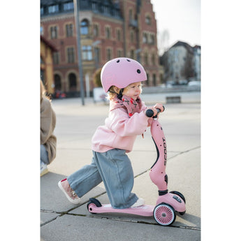 Toddler in pink helmet and sweatshirt riding a pink Scoot & Ride Highwaykick 1 scooter.