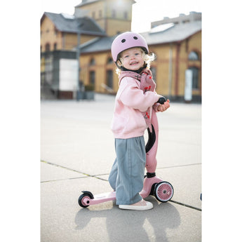 Happy toddler in pink helmet and outfit with a pink Scoot & Ride Highwaykick 1 scooter.