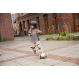 Child in helmet and pads riding a white Scoot & Ride Highwaykick 3S LED 3-wheel scooter outdoors.