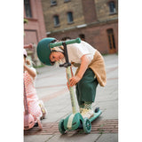 Child in green helmet adjusts a mint green Scoot & Ride Highwaykick 3S LED 3-wheel scooter.