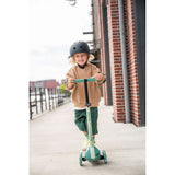 Smiling child in a helmet riding a green Scoot & Ride Highwaykick 3S LED 3-wheel light-up scooter.
