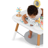 Baby in a white Skip Hop Discoverosity 3-Stage Activity Center with wooden legs and colorful toys.