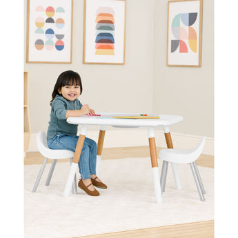Happy child at a white and natural wood Skip Hop activity table with two matching chairs.