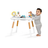 Happy baby playing with a white Skip Hop Discoverosity activity center with wooden legs and colorful toys.