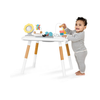 Happy baby playing with a white Skip Hop Discoverosity activity center with wooden legs and colorful toys.