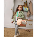 Young girl holds a peach Skip Hop Duffimals duffle bag with a cute cat face and mint green strap.