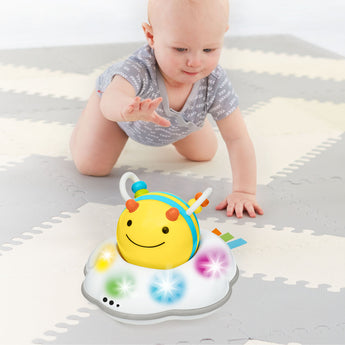 Baby crawling towards a yellow and blue Skip Hop Follow Bee toy with colorful lights on a grey playmat.