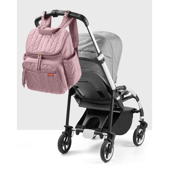 Pink quilted Skip Hop Forma backpack nappy bag hanging from a gray stroller handle.