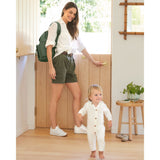 Woman in white shirt and shorts wearing a dark green quilted Skip Hop Forma backpack, with a toddler.