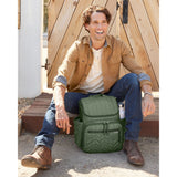 Man sitting outdoors with a green quilted Skip Hop Forma backpack, featuring side pockets and a water bottle.