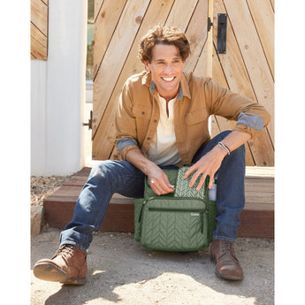 Smiling man opening a green quilted Skip Hop Forma backpack with a geometric packing cube.