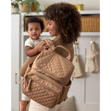 Woman carrying baby and a stylish tan quilted Skip Hop Forma backpack nappy bag with gold zippers.