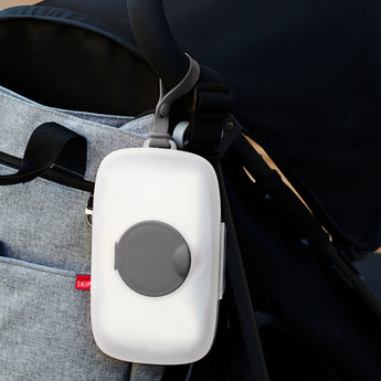 White Skip Hop Grab & Go Wipes Case with gray seal and strap, hanging from a black stroller handle.