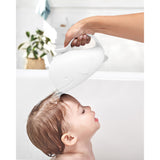 White whale-shaped Skip Hop Moby Waterfall Rinser pouring water over a baby's head in a bathtub.