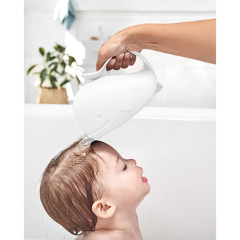 White whale-shaped Skip Hop Moby Waterfall Rinser pouring water over a baby's head in a bathtub.