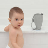 Cute baby looking at the camera next to a gray whale-shaped Skip Hop Moby Waterfall Rinser on a white marble ledge.