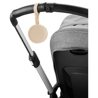 Beige Skip Hop silicone pacifier holder with a flower design, attached to a black stroller handle.