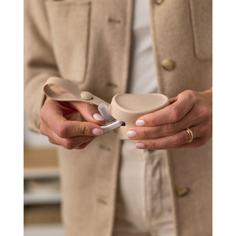 Hands holding a beige Skip Hop silicone pacifier holder with a pacifier partially inserted.