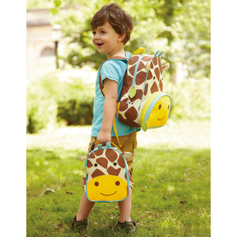 Smiling boy wearing a brown and white giraffe Skip Hop Zoo Backpack, holding a matching lunch bag.