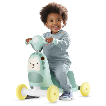 Happy toddler riding a mint green Skip Hop Zoo 3-in-1 hedgehog ride-on toy with yellow wheels.