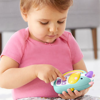 Baby in pink shirt playing with a light blue Skip Hop Zoo Phone unicorn toy with a light-up horn and colorful buttons.