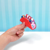 Hand holding a red slime taco filled with colorful, swirled slime, sprinkles, and blueberries against a blue striped background.