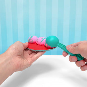 Hands holding a red plate with three pink and green slime balls, using a teal scoop.