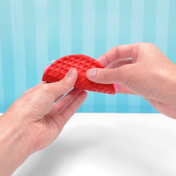 Hands holding a red, textured taco-shaped slime toy with pink and green slime filling.