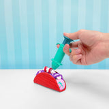 Hand using a teal syringe to fill a red silicone taco shell with colorful, rolled slime.