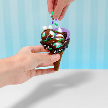 Hands hold a brown slime ice cream cone with chocolate, purple, and mint slime, topped with colorful sprinkles.