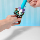 Hands decorating a brown slime ice cream cone with purple, teal, and white slime scoops, sprinkles, and chocolate drizzle.