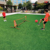 Two boys playing Soccer Tennis with an orange KickerBall net and red soccer ball on green artificial turf.