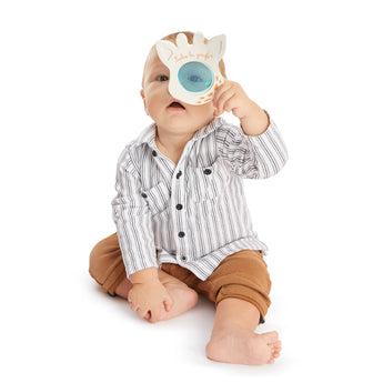 Baby holding a white Sophie la girafe Magic Mirror SIGHT teething toy over one eye.