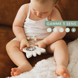 Baby holds a white Sophie la girafe Magic Mirror SIGHT teething toy with black patterns.