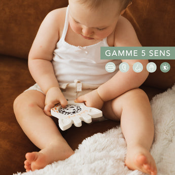 Baby holds a white Sophie la girafe Magic Mirror SIGHT teething toy with black patterns.