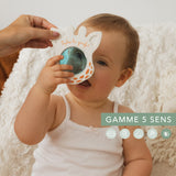 Baby holding a white Sophie la girafe Magic Mirror Teething Toy with orange polka dots.