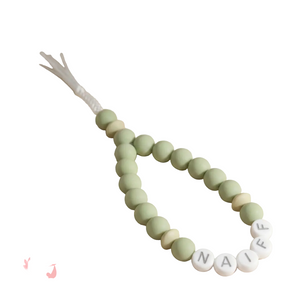 Green teething necklace with name beads on a beige background